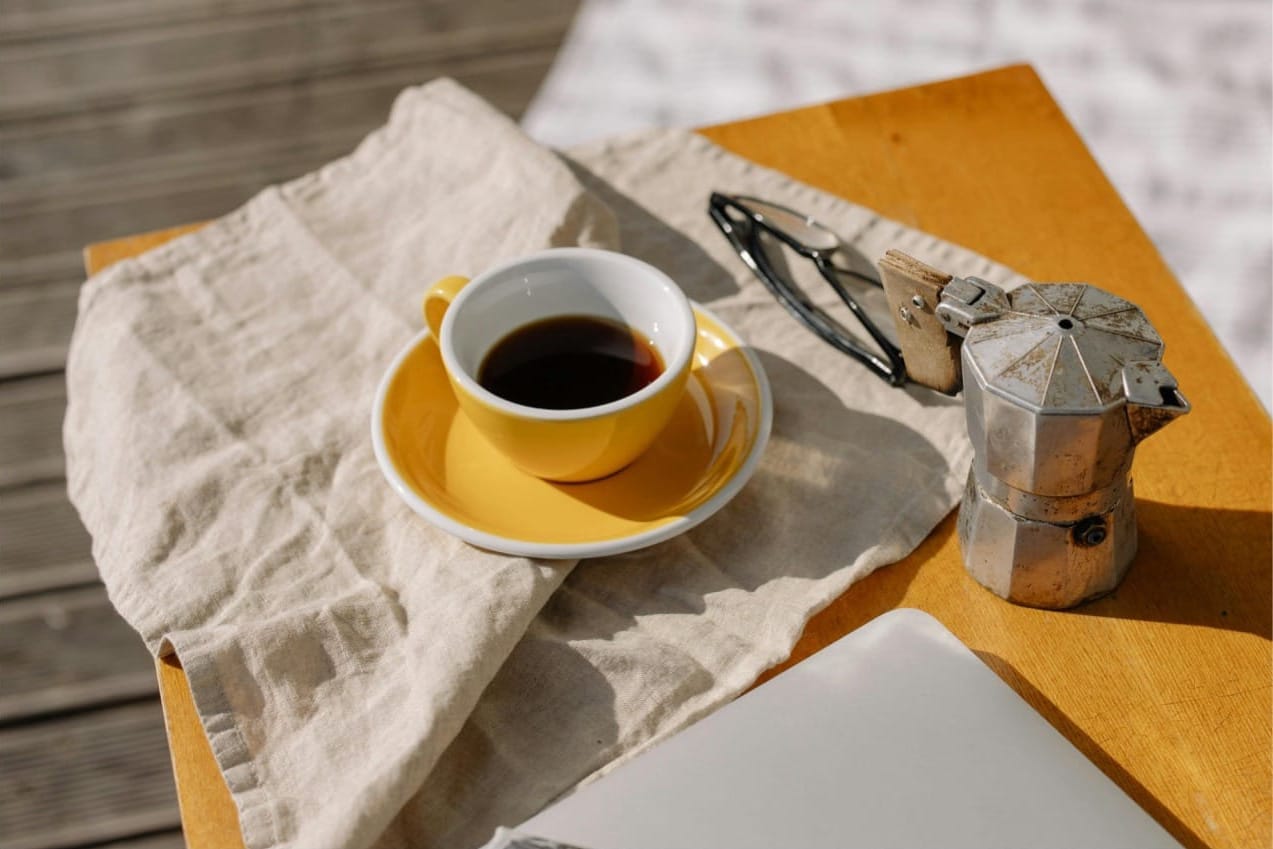 Une tasse de café, près d'une cafetière italienne et d'un ordinateur